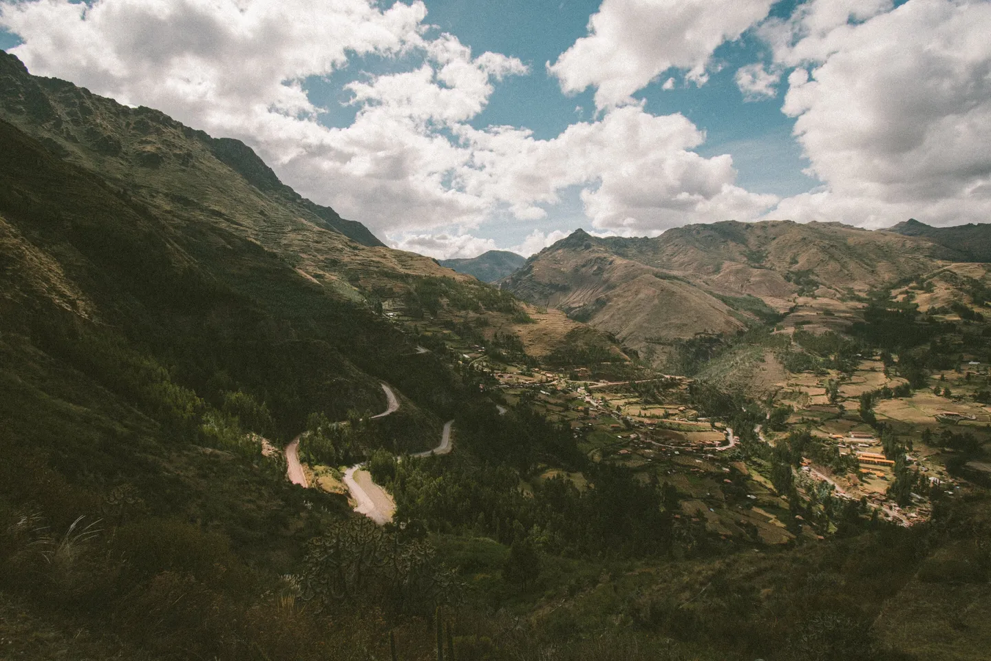 Green valley and fields in Cusco, Perú, with scattered buildings.